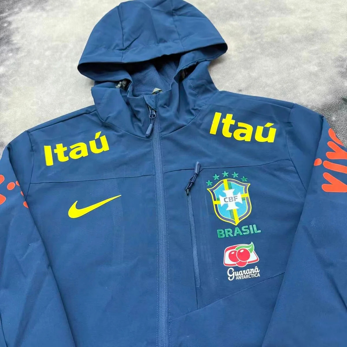 Détail buste de la veste imperméable bleue du Brésil, poche zippée et écussons jaunes sur les épaules